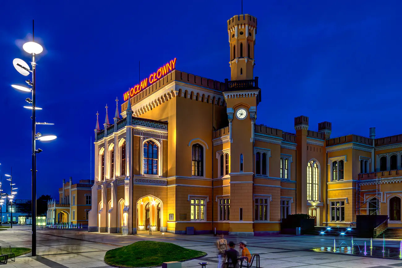 Wrocław Dworzec Główny nocą, podświetlona neogotycka elewacja i pusty plac przed wejściem